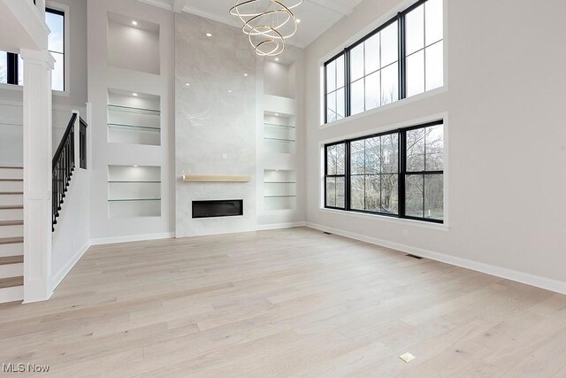 unfurnished living room featuring built in shelves, a fireplace, light wood-style flooring, and baseboards