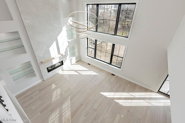 unfurnished living room featuring a chandelier, a high ceiling, wood finished floors, and baseboards