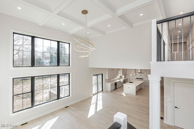 living area featuring light wood-style flooring, a high ceiling, coffered ceiling, visible vents, and beamed ceiling