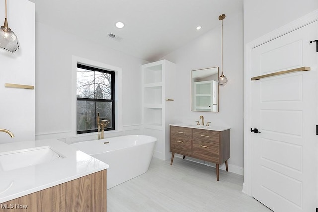 bathroom with a soaking tub, visible vents, two vanities, and a sink