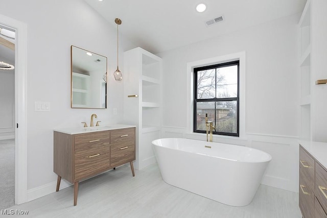 bathroom featuring a decorative wall, a wainscoted wall, visible vents, vanity, and a soaking tub