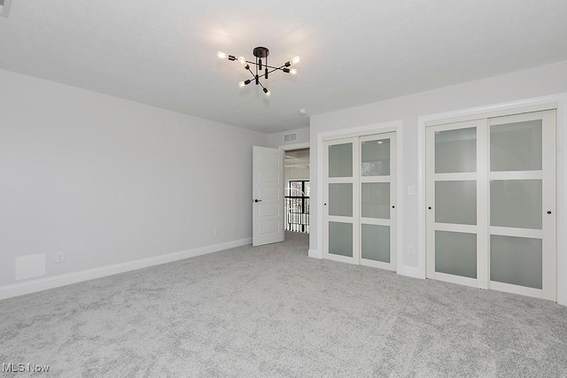 carpeted empty room featuring baseboards, visible vents, and an inviting chandelier