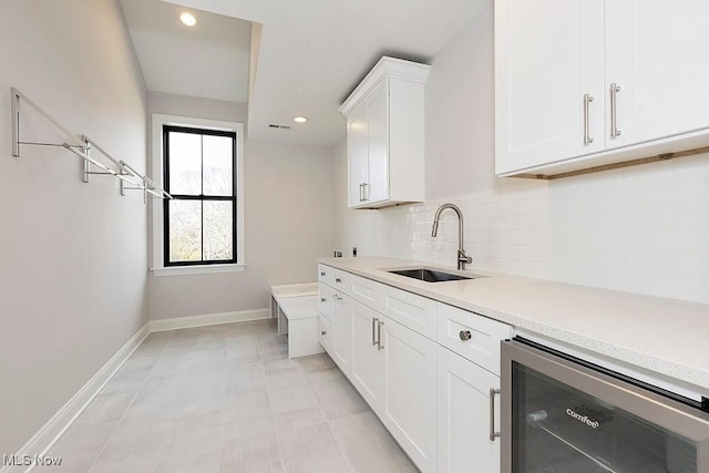 kitchen featuring beverage cooler, baseboards, a sink, light countertops, and backsplash