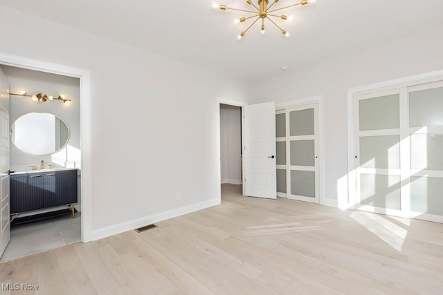 unfurnished bedroom featuring a chandelier, ensuite bathroom, visible vents, baseboards, and light wood-type flooring