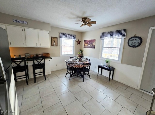 tiled dining room with ceiling fan and a textured ceiling