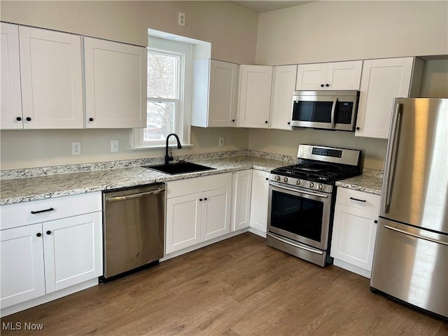 kitchen with dark hardwood / wood-style floors, sink, white cabinetry, light stone countertops, and appliances with stainless steel finishes