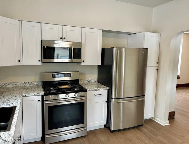 kitchen with white cabinetry, stainless steel appliances, sink, light stone counters, and light hardwood / wood-style flooring