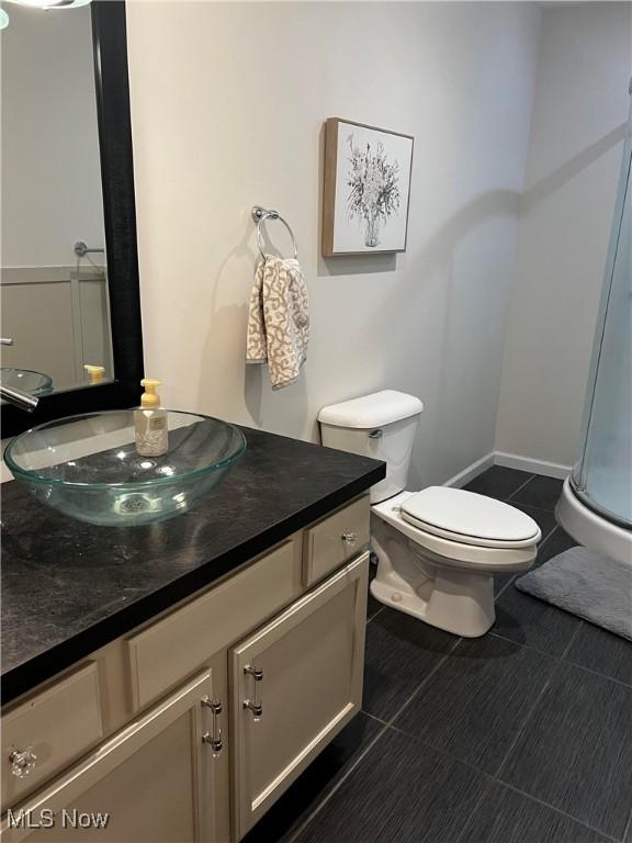 bathroom featuring a shower with shower door, vanity, tile patterned flooring, and toilet