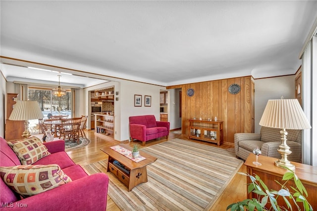 living room with light hardwood / wood-style flooring, a notable chandelier, and wooden walls