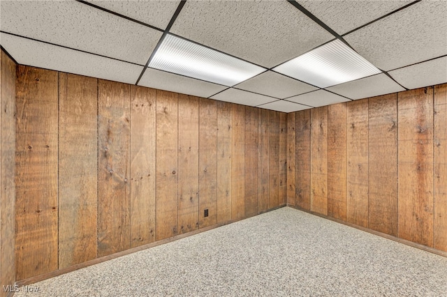 basement with carpet floors, a paneled ceiling, and wood walls