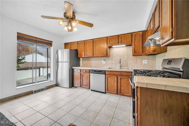 kitchen featuring ceiling fan, stainless steel appliances, tile counters, light tile patterned flooring, and sink