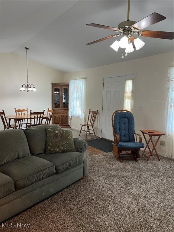 living room with ceiling fan with notable chandelier, dark carpet, and vaulted ceiling