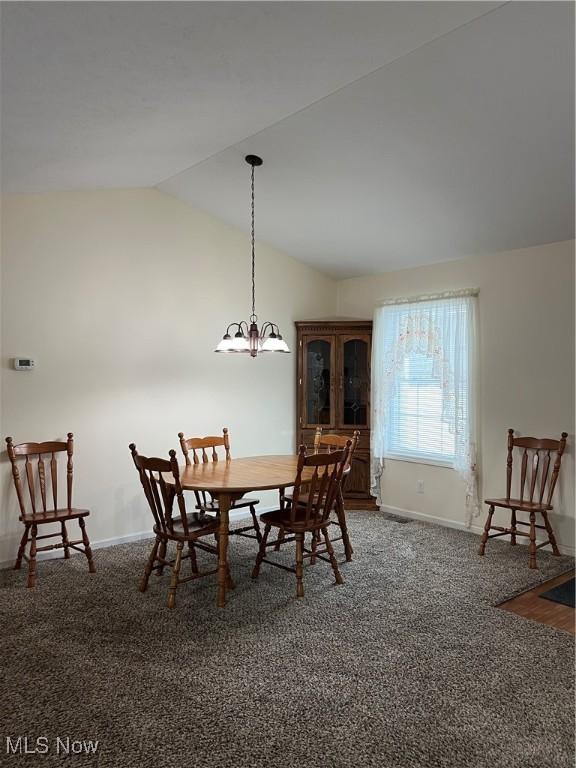 carpeted dining room with vaulted ceiling and a notable chandelier