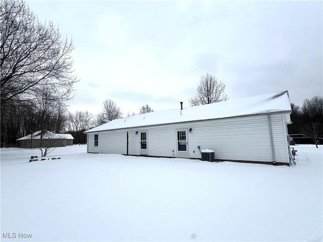 snow covered rear of property featuring central AC unit