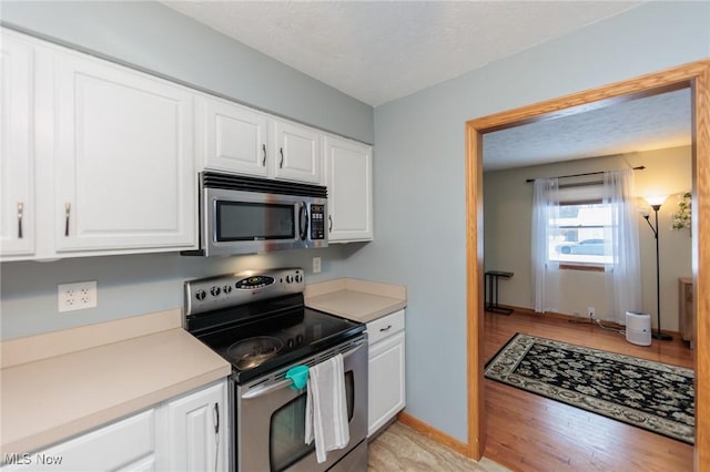 kitchen with light hardwood / wood-style floors, white cabinetry, appliances with stainless steel finishes, and a textured ceiling