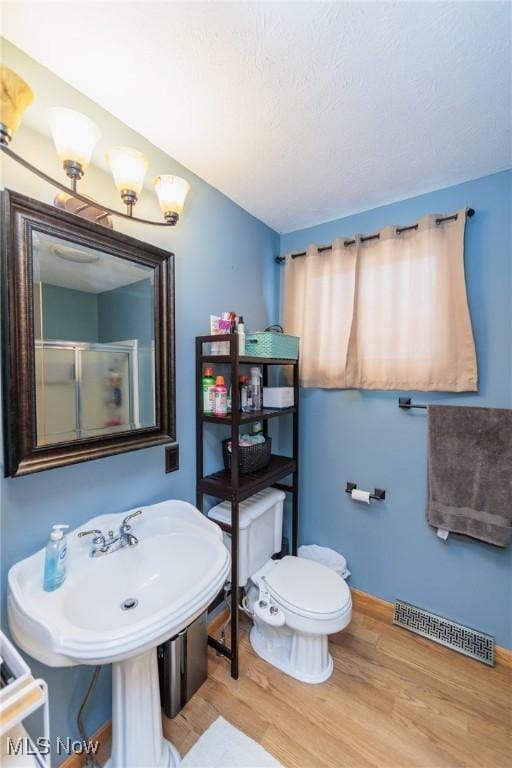 bathroom with hardwood / wood-style flooring, sink, toilet, and a shower with shower door