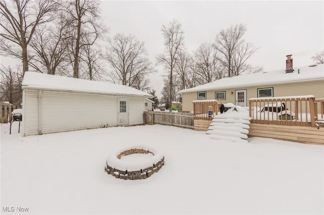 snow covered back of property with a deck and an outdoor fire pit