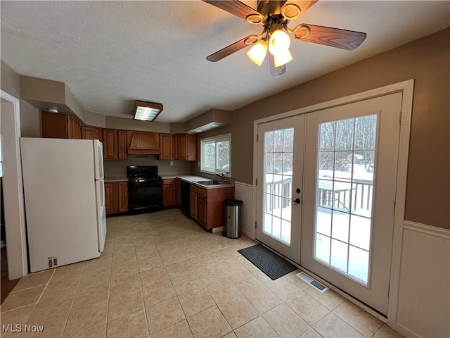 kitchen with white refrigerator, french doors, sink, black range, and ceiling fan