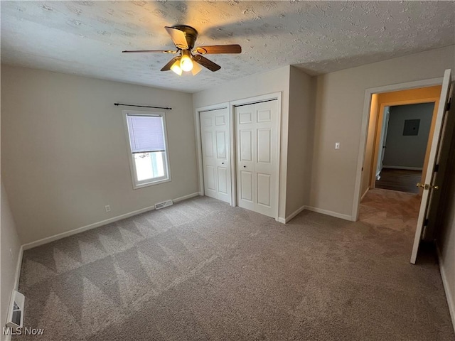 unfurnished bedroom featuring ceiling fan, two closets, a textured ceiling, and carpet floors