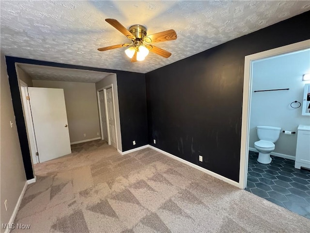 unfurnished bedroom featuring a textured ceiling, ensuite bath, carpet floors, a closet, and ceiling fan