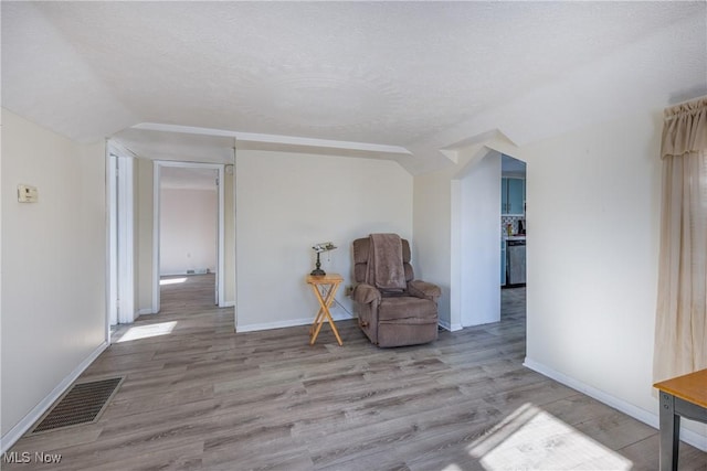 living area featuring a textured ceiling, light wood-type flooring, and vaulted ceiling