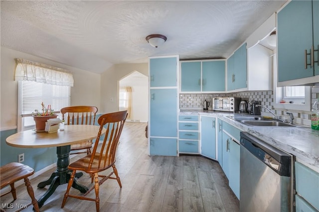 kitchen featuring blue cabinetry, backsplash, vaulted ceiling, stainless steel dishwasher, and sink