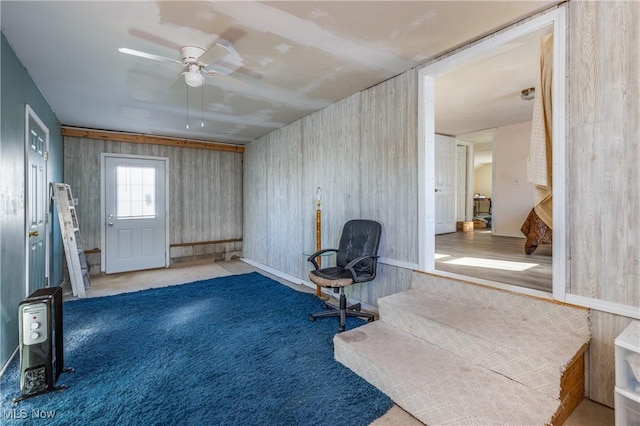 sitting room with ceiling fan, light colored carpet, and wood walls