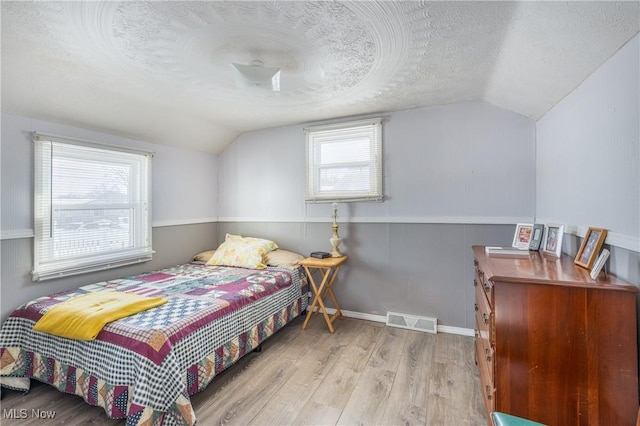 bedroom with lofted ceiling, a textured ceiling, and light hardwood / wood-style flooring