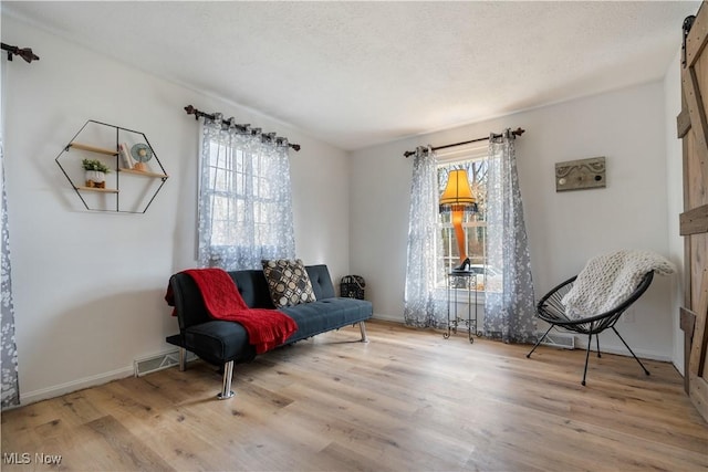 sitting room featuring a textured ceiling, a barn door, and light wood-type flooring