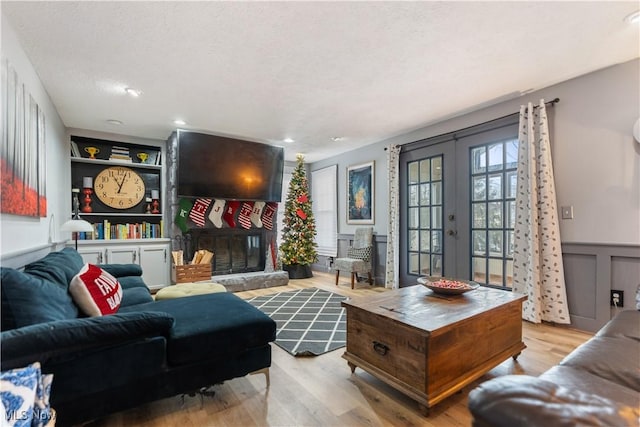 living room featuring french doors, a textured ceiling, a fireplace, and light hardwood / wood-style flooring