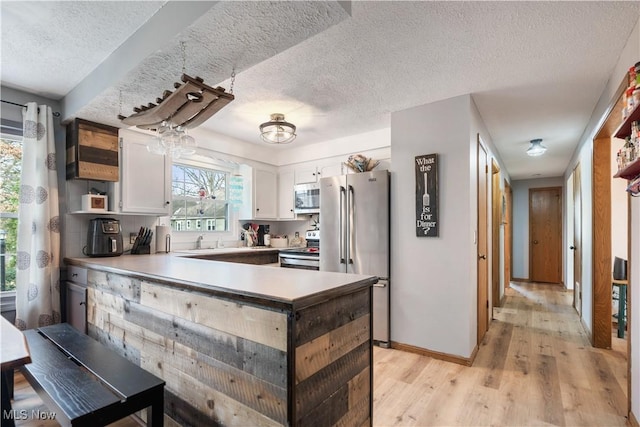 kitchen with a textured ceiling, white cabinetry, stainless steel appliances, light hardwood / wood-style floors, and kitchen peninsula