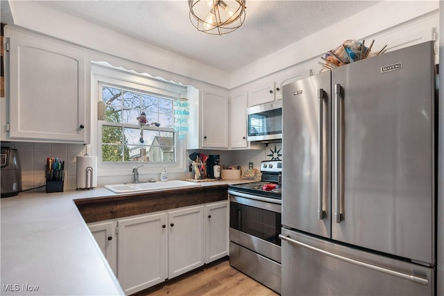 kitchen with backsplash, sink, light wood-type flooring, stainless steel appliances, and white cabinets