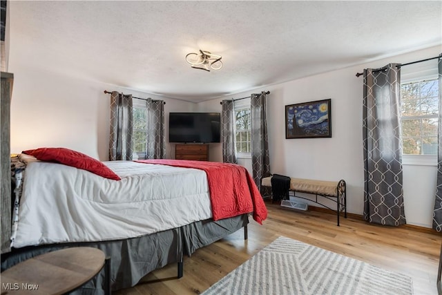 bedroom featuring multiple windows, light hardwood / wood-style flooring, and a textured ceiling