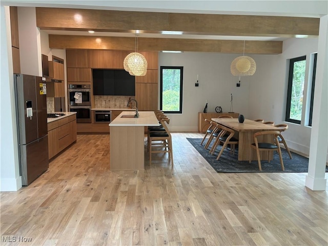 kitchen with an island with sink, appliances with stainless steel finishes, backsplash, hanging light fixtures, and beam ceiling