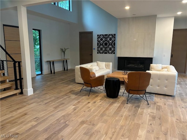 living room with light wood-type flooring, a towering ceiling, and a fireplace