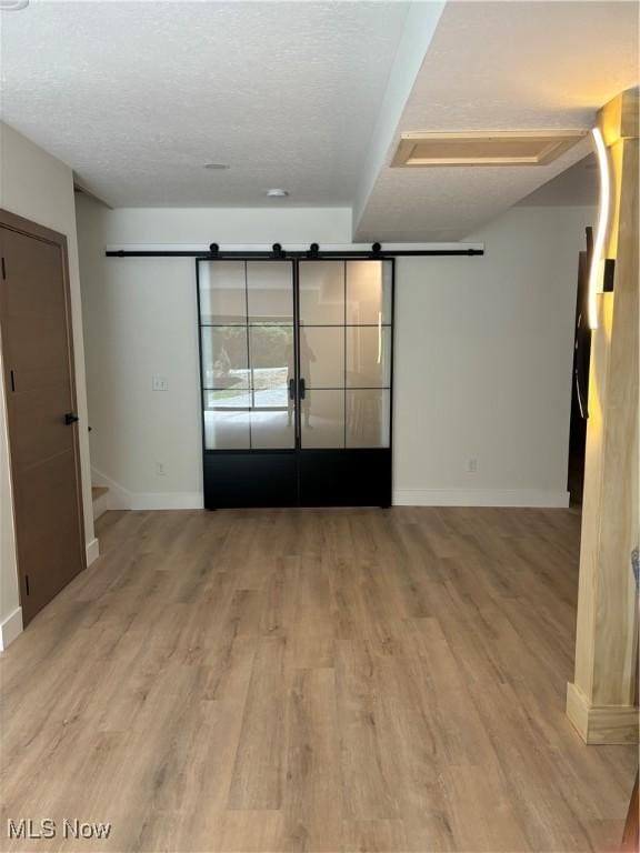 spare room featuring a textured ceiling, light hardwood / wood-style flooring, and a barn door