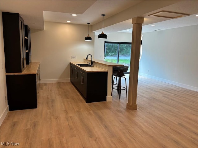 kitchen featuring sink, hanging light fixtures, kitchen peninsula, light wood-type flooring, and a breakfast bar