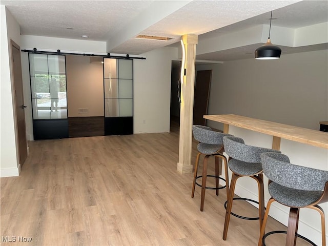 interior space featuring a textured ceiling, light hardwood / wood-style floors, a barn door, and french doors