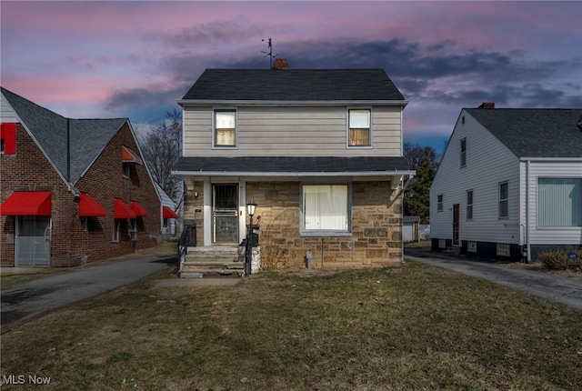 traditional-style home featuring stone siding, a chimney, and a yard