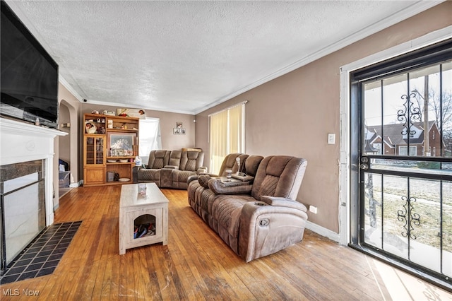 living area with hardwood / wood-style floors, arched walkways, ornamental molding, a textured ceiling, and a tiled fireplace