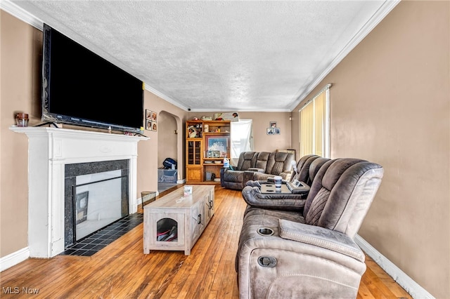 living area featuring crown molding, arched walkways, light wood finished floors, and a tile fireplace