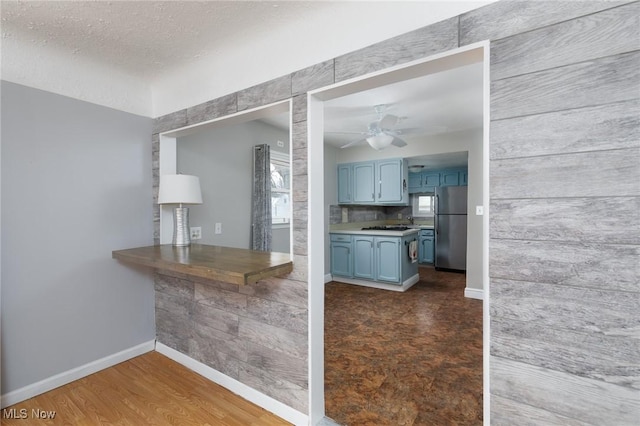 kitchen with ceiling fan, backsplash, dark hardwood / wood-style flooring, blue cabinets, and stainless steel fridge