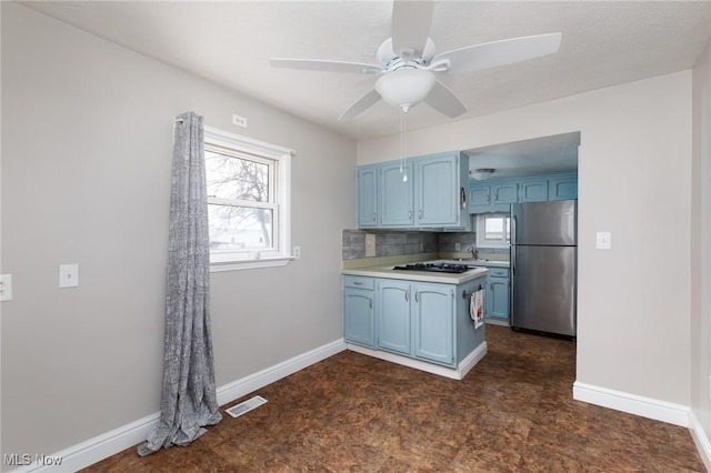 kitchen featuring ceiling fan, tasteful backsplash, gas stovetop, blue cabinets, and stainless steel refrigerator