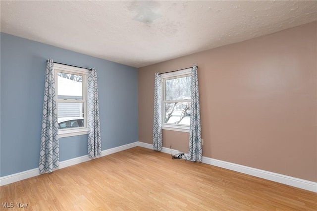 spare room featuring light wood-type flooring, a wealth of natural light, and a textured ceiling