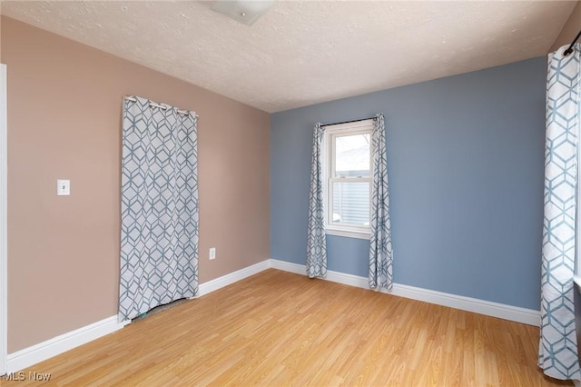 empty room with a textured ceiling and light hardwood / wood-style flooring