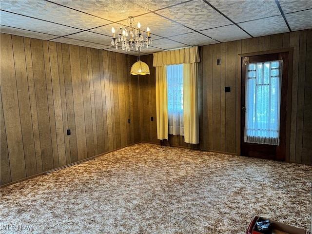 carpeted empty room featuring a notable chandelier and wood walls