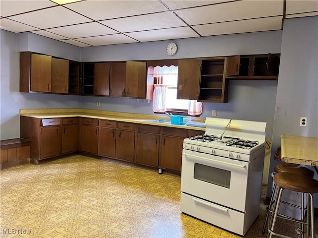 kitchen with a kitchen bar, dark brown cabinets, white range with gas stovetop, and sink