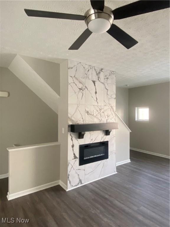 unfurnished living room featuring ceiling fan, a textured ceiling, dark hardwood / wood-style floors, and a tile fireplace