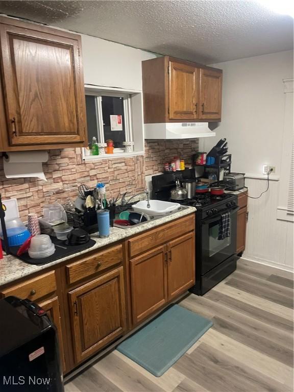 kitchen with decorative backsplash, black gas stove, light hardwood / wood-style flooring, and a textured ceiling