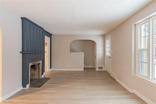 unfurnished living room with light wood-type flooring, a large fireplace, and a textured ceiling